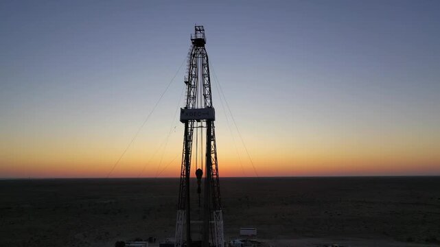 Oil drilling rig silhouette at sunset in desert oilfield.