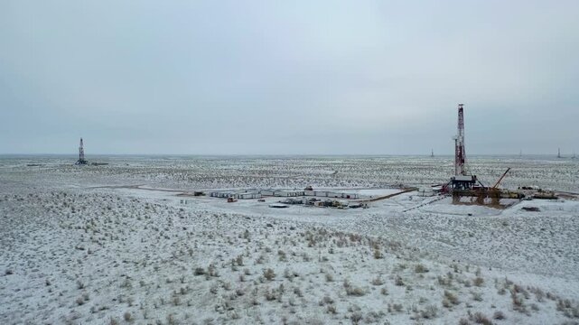 Remote drilling rig standing in snowy gas field under overcast sky.
