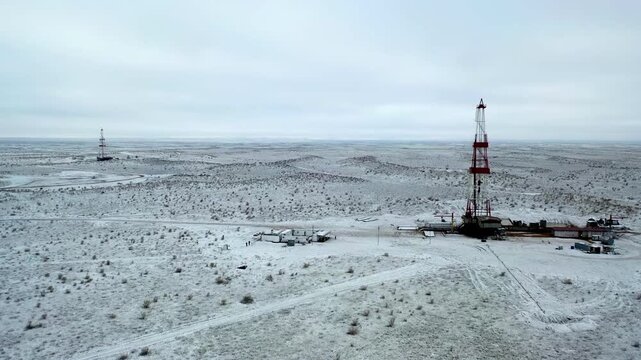 Snow-covered gas field with drilling rig in cold winter environment.