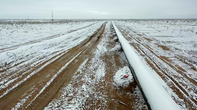 Snow-covered industrial road leading through remote gas field.