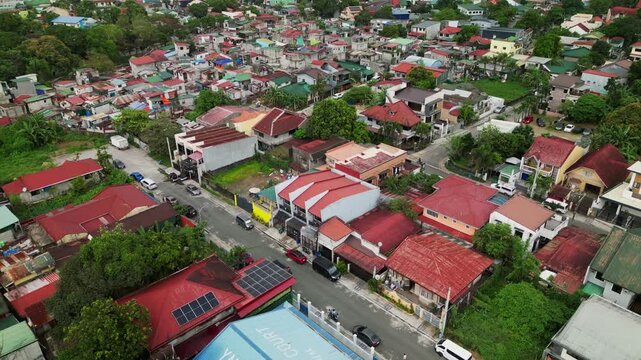 Rising aerial shot of a residential neighborhood with red rooftops, busy streets, and surrounding greenery in Antipolo City, Rizal, Philippines.