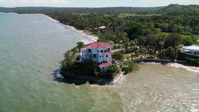 Aerial orbit of Roca Encantada, a historic seaside mansion on a small peninsula surrounded by ocean and lush greenery in Guimaras, Philippines.