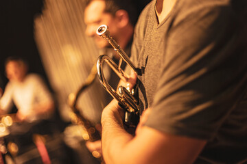 Trumpet player holding instrument on stage with band © Filipo