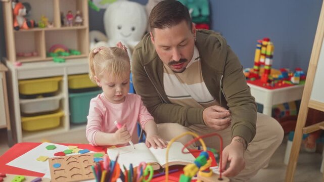 Man guides girl's hand holding a marker over a workbook in a playroom building; learning bonding warmth.