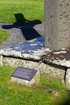 View of the stone base and plaque of St John's Cross replica with its shadow cast on the grass at the historic Iona Abbey and Nunnery in Isle of Iona, Scotland, United Kingdom.