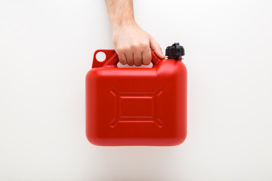 Young adult man hand holding 5L red plastic canister for car petrol on light gray wall background. Closeup. Front view.