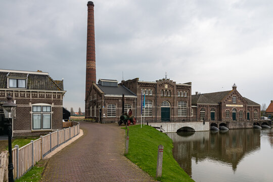 View of the Dutch Steam Engine Museum with its tall brick chimney and historic industrial architecture by the water in Medemblik, Noord-Holland, Netherlands.