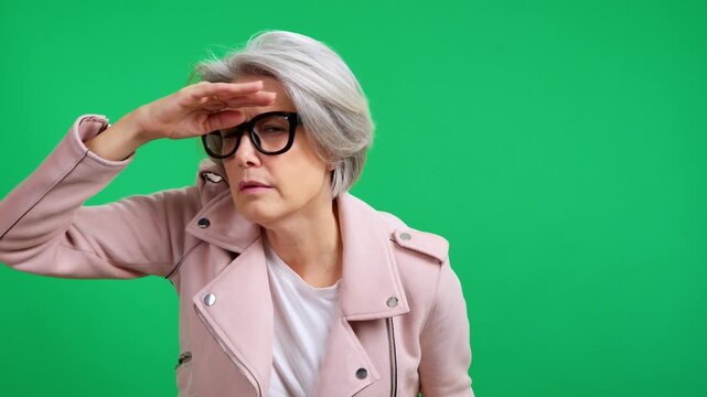Senior woman with glasses searching and looking far away on a green background