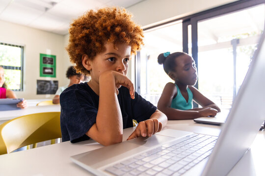 Diverse elementary students working on laptops and tablets at classroom desks with yellow chairs