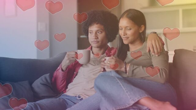 Couple sitting on sofa woman pointing offcam for romance man raising mug leaning with heart overlay