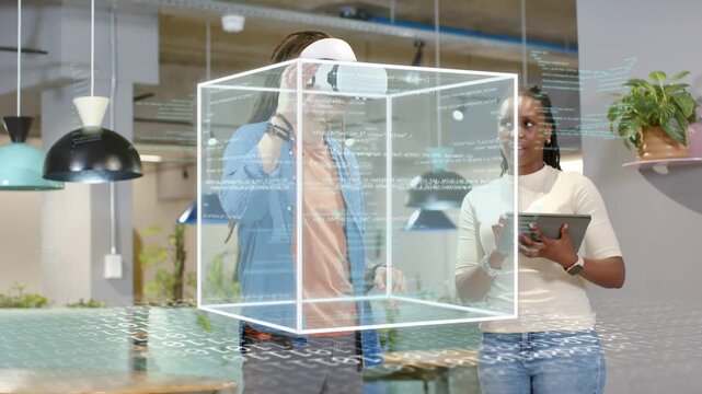 Woman tapping tablet initiating tech demo while man wearing VR headset manipulating wireframe cube