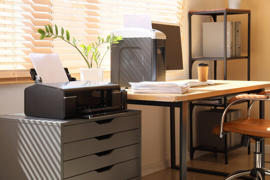Modern workplace with shredder, documents and printer near window in office
