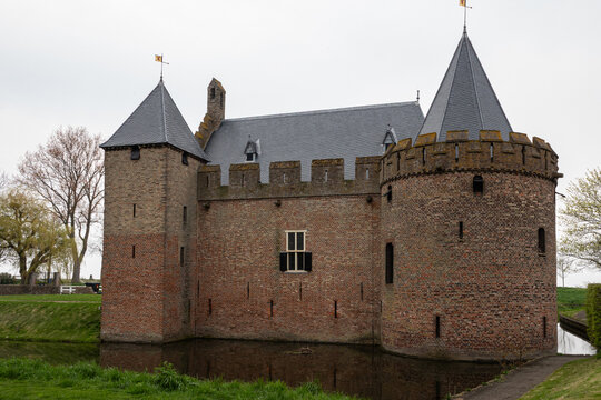 View of Radboud Castle featuring medieval brick walls, towers, battlements, and a moat under an overcast sky in Medemblik, Noord-Holland, Netherlands.