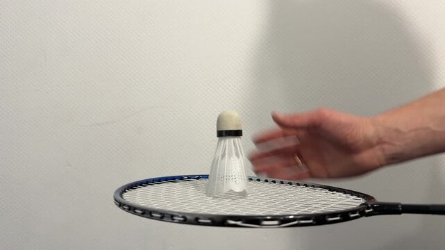 Close up of hand placing shuttlecock on racket, preparing for badminton hit, sport equipment interaction concept