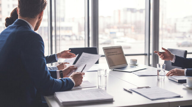 Business people's hands working on documents and laptop at a modern office table with city view.
