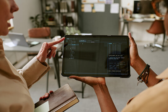 Close up of diverse women reviewing software code on tablet, discussing app development in office. Ideal for technology teamwork, coding education, digital product design