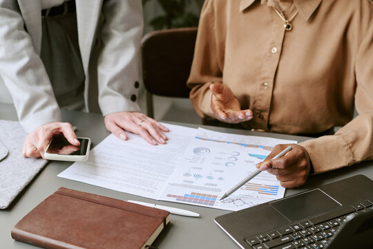 Close up of businesswomen reviewing analytics report, pointing at charts, discussing strategy during meeting. Ideal for teamwork, financial planning, consulting, corporate communication