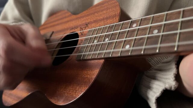 Man strumming ukulele strings close up at home, playing music, rhythm practice, creative hobby activity, musical performance