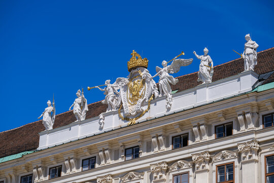 View of the Hofburg palace roofline featuring white statues and a golden coat of arms under a clear blue sky in Vienna, Vienna, Austria.