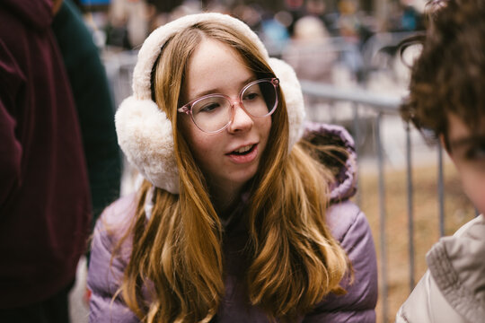 Teen girl in glasses and earmuffs talking to companion