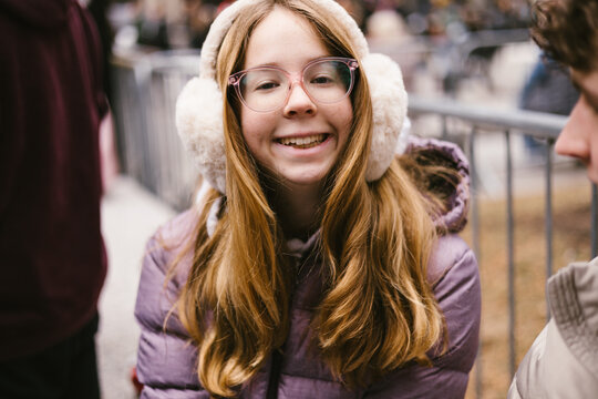 Blond young teen girl in earmuffs outside in city in winter