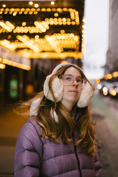 Teen girl in earmuffs outside muffs and coat in city lights