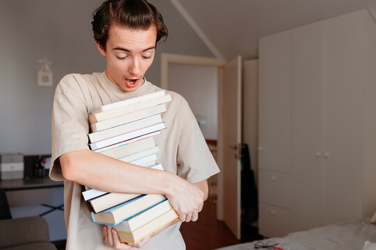 Overwhelmed young student carrying massive stack of books