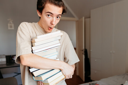 Shocked teenage boy with heavy pile of school textbooks