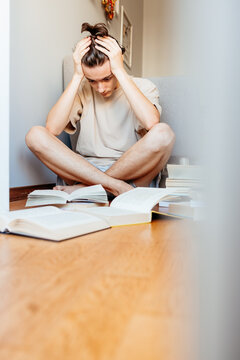 Stressed young person holding head while studying with open books