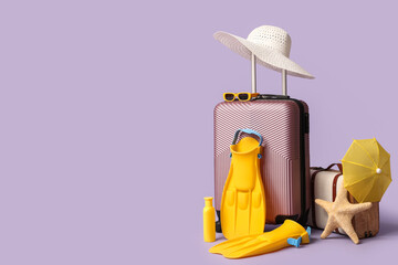 Suitcases, beach accessories, sunscreen and decor on lilac background © Pixel-Shot
