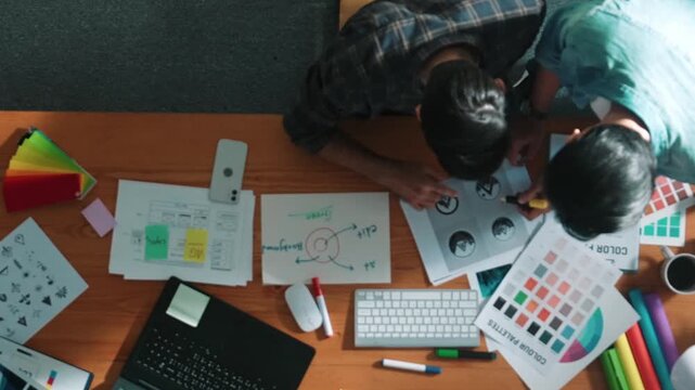 Top down view of smart designer helping manager choosing color from colored palettes. Aerial view of businessman working together and planning together while looking at logo from laptop. Symposium.