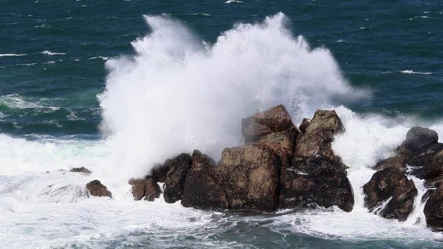 Powerful ocean waves crash against rugged rocks under a clear sky, showcasing nature's force. Ideal for use in oceanic documentaries or weather-related content.Sinemorets, Burgas, Bulgaria