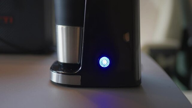 Close-up of a hand pressing the power button on a small portable coffee machine. Minimal lifestyle scene highlighting convenience, travel brewing, and modern coffee technology.