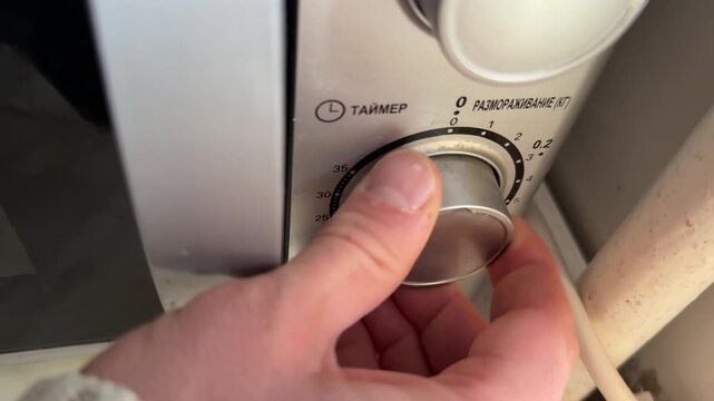 Person turning microwave control knob close up at home, setting time or power level, kitchen appliance use, cooking process concept