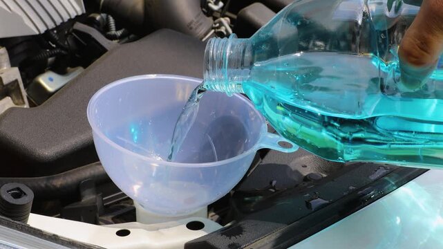自動車のボンネットを開けてウィンドウォッシャー液を補充している	