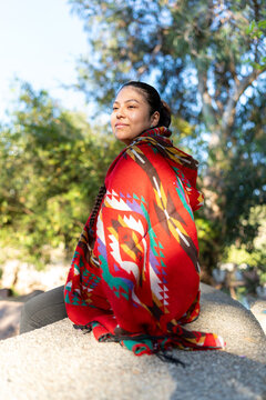 Indigenous Peruvian woman sitting in park wearing colorful traditional poncho