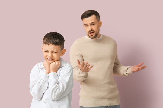 Upset boy and his father squabbling on pink background