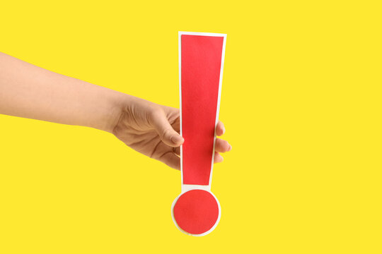 Female hand with red paper exclamation mark on yellow background, closeup