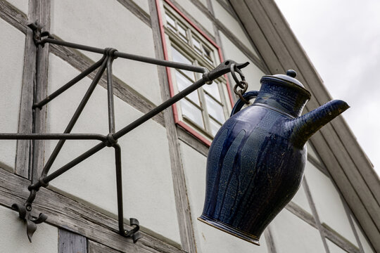 View of a blue ceramic pitcher hanging from a wrought iron sign bracket on a traditional half-timbered house at the Hennebergisches Museum, Kloster Vessra, Thuringen, Germany.