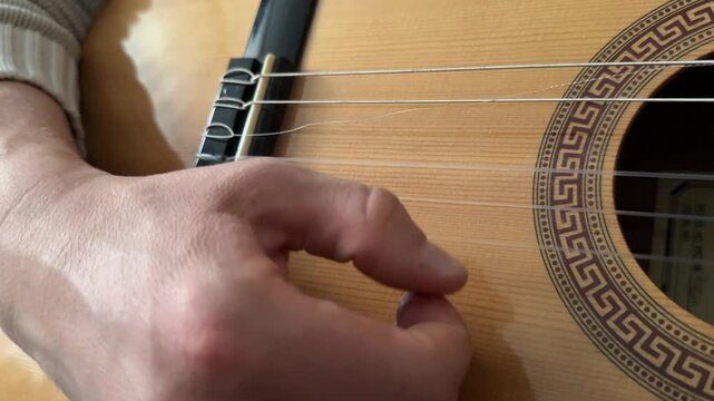 Close-up of a man playing an acoustic guitar. The frame shows the fretboard and the musician's hand