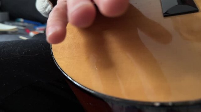 Person hitting acoustic guitar body with palm close up at home, producing strong rhythmic percussion sound, improvised music activity, creative hobby concept