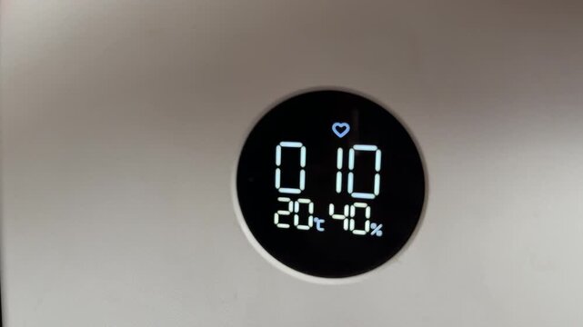 Round digital display showing temperature and humidity levels, smart home environment monitoring device, minimal modern design with illuminated interface