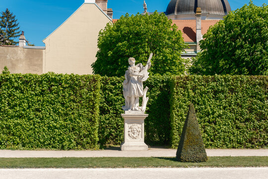View of a classical marble statue playing a lute in the manicured gardens of the Belvedere Palace under a clear blue sky in Vienna, Vienna, Austria.