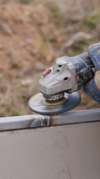 Metal Grinder Smoothing Steel Edge Outdoors With Gloved Hands, Closeup Of Abrasive Disc Producing Dust And Sparks, Jacketed Operator Refining Seam, Finishing And Deburring On Construction