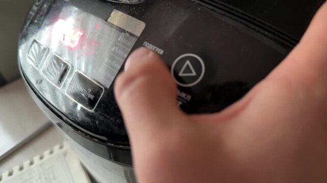 Person pressing button on multicooker control panel close up at home, starting cooking program, kitchen appliance use concept