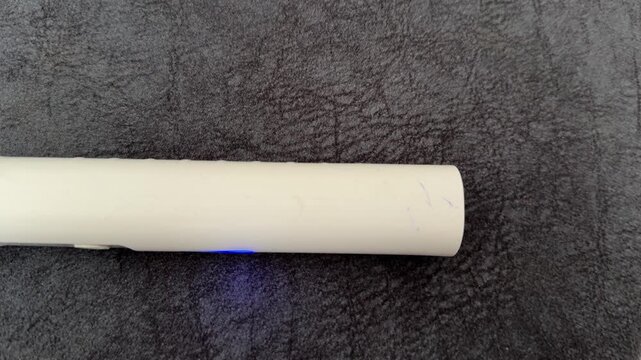 electric toothbrush handle with blue indicator light in close up, rechargeable dental care device