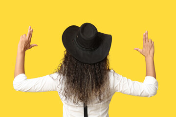Obraz premium Beautiful African-American cowgirl making guns with her hands on yellow background, back view