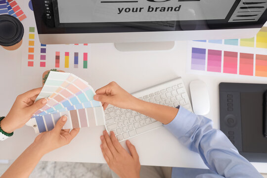 Female graphic designers working with color palettes at table in office, top view