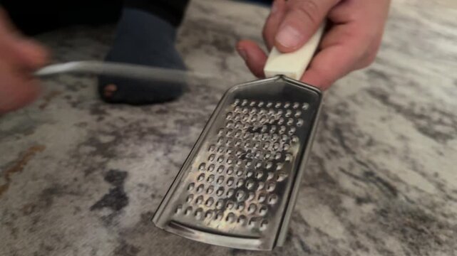 Person tapping metal grater with fork close up at home, producing rhythmic sound, improvised percussion activity, creative hobby concept