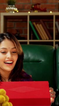 Friends video calling on Diwali, Indian Asian young married couples in traditional festive wear celebrating Deepavali at decorated home holding laddu barfi sweets and attending smartphone video call